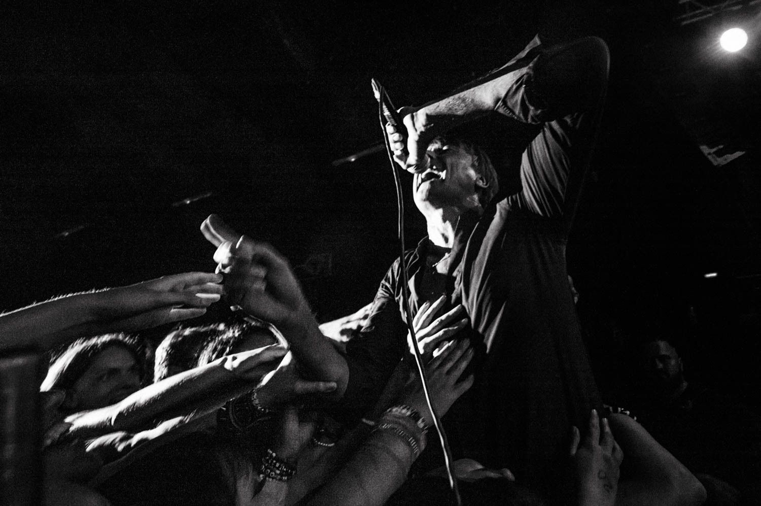 Brett Anderson from Suede singing to the Warsaw audience as many of them place their hands on him from the crowd. Photograph of a high-energy moment in black and white.